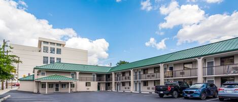 A motel with a green roof, multiple balconies, and a parking lot with several cars.