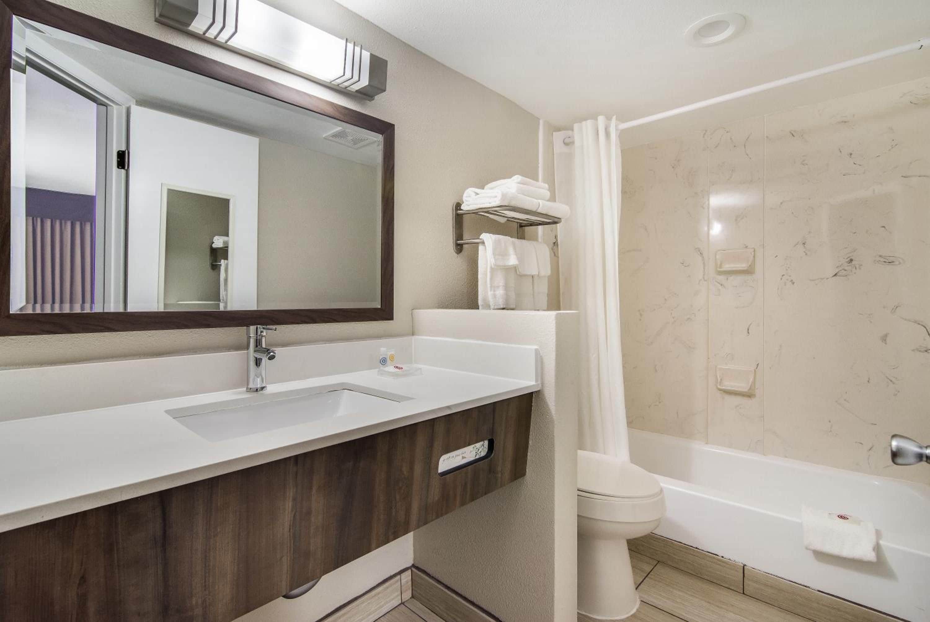 A modern bathroom with a large mirror, a sink, a toilet, and a shower area.