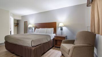 Een hotelkamer met een groot bed, twee bedlampen, een houten nachtkastje, een stoel en een deur naar een inloopkast.