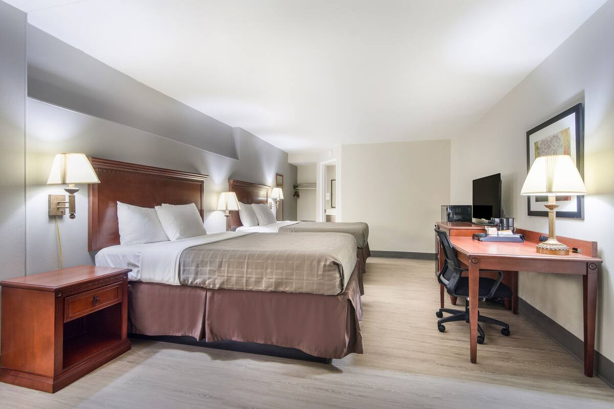 A hotel room with two beds, a desk, and a TV.