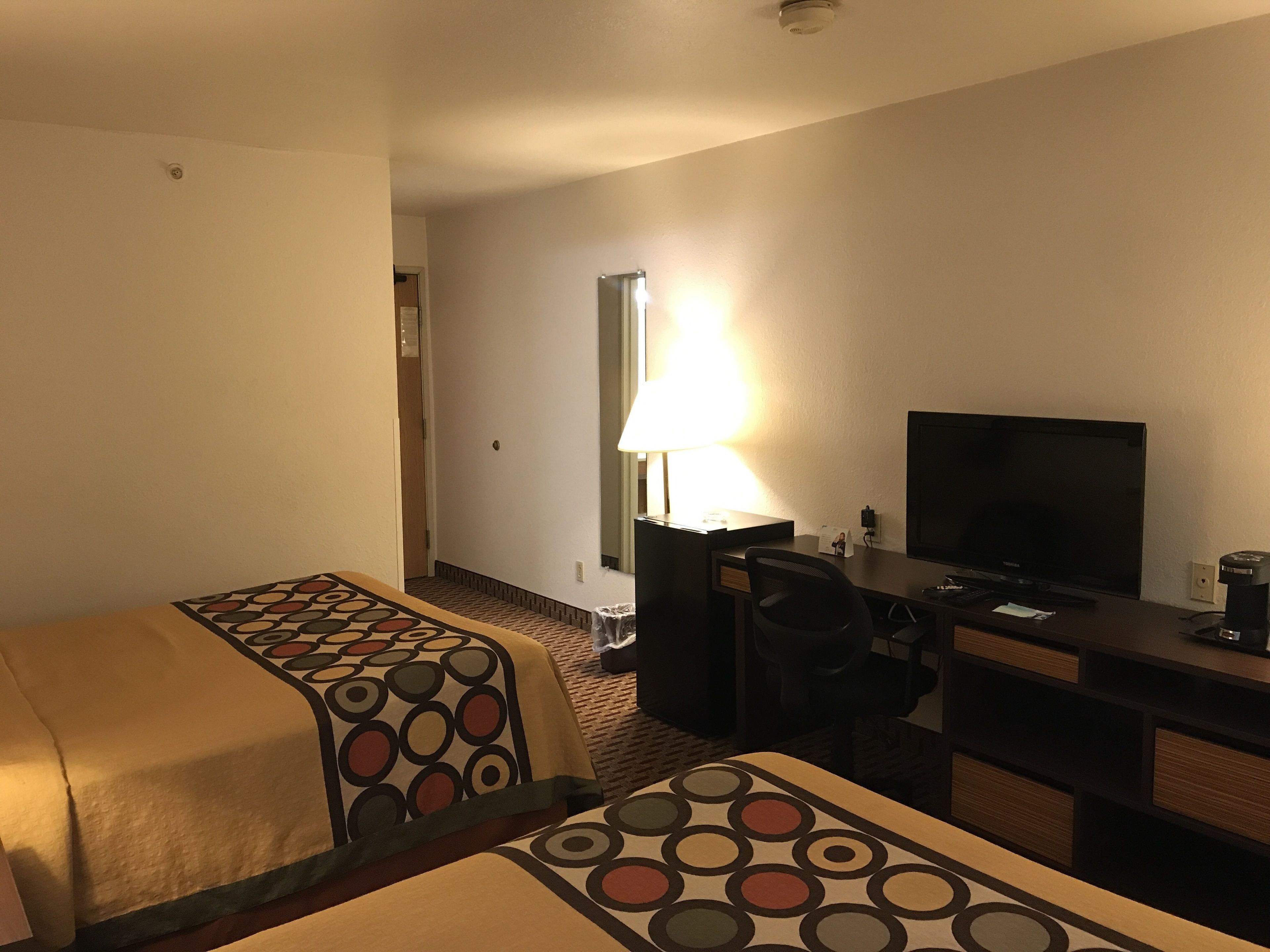 A hotel room with two beds, a desk, a chair, a television, and a lamp.