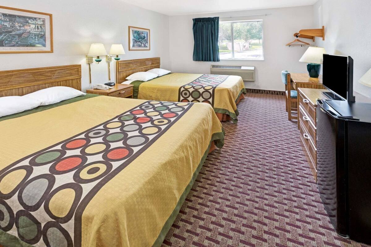 Habitación de hotel con dos camas, un escritorio, un televisor y una ventana con cortinas.