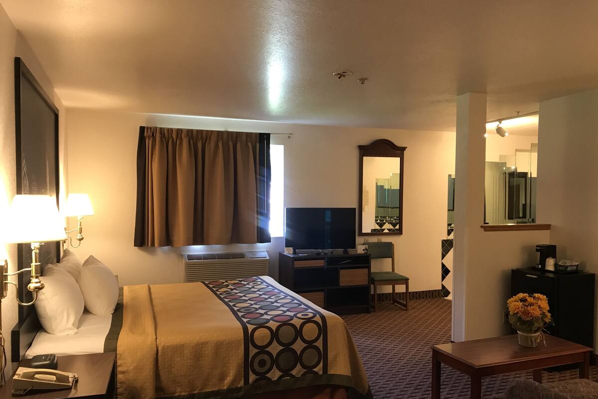 Habitación de hotel con cama, escritorio, televisor, espejo y una mesita con flores.