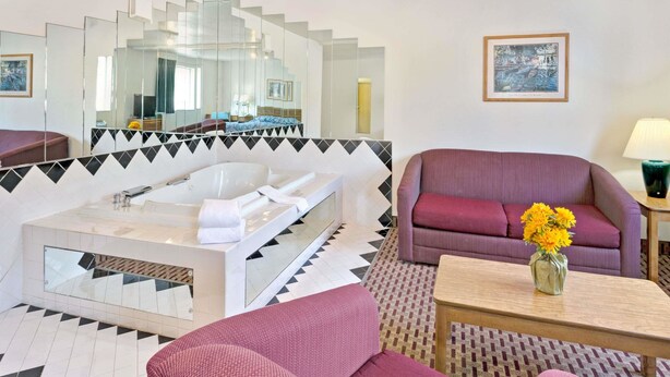 Een moderne hotelkamer met een grote spiegel, een badkuip, een bank en een bijzettafeltje met een bloemenvaas.