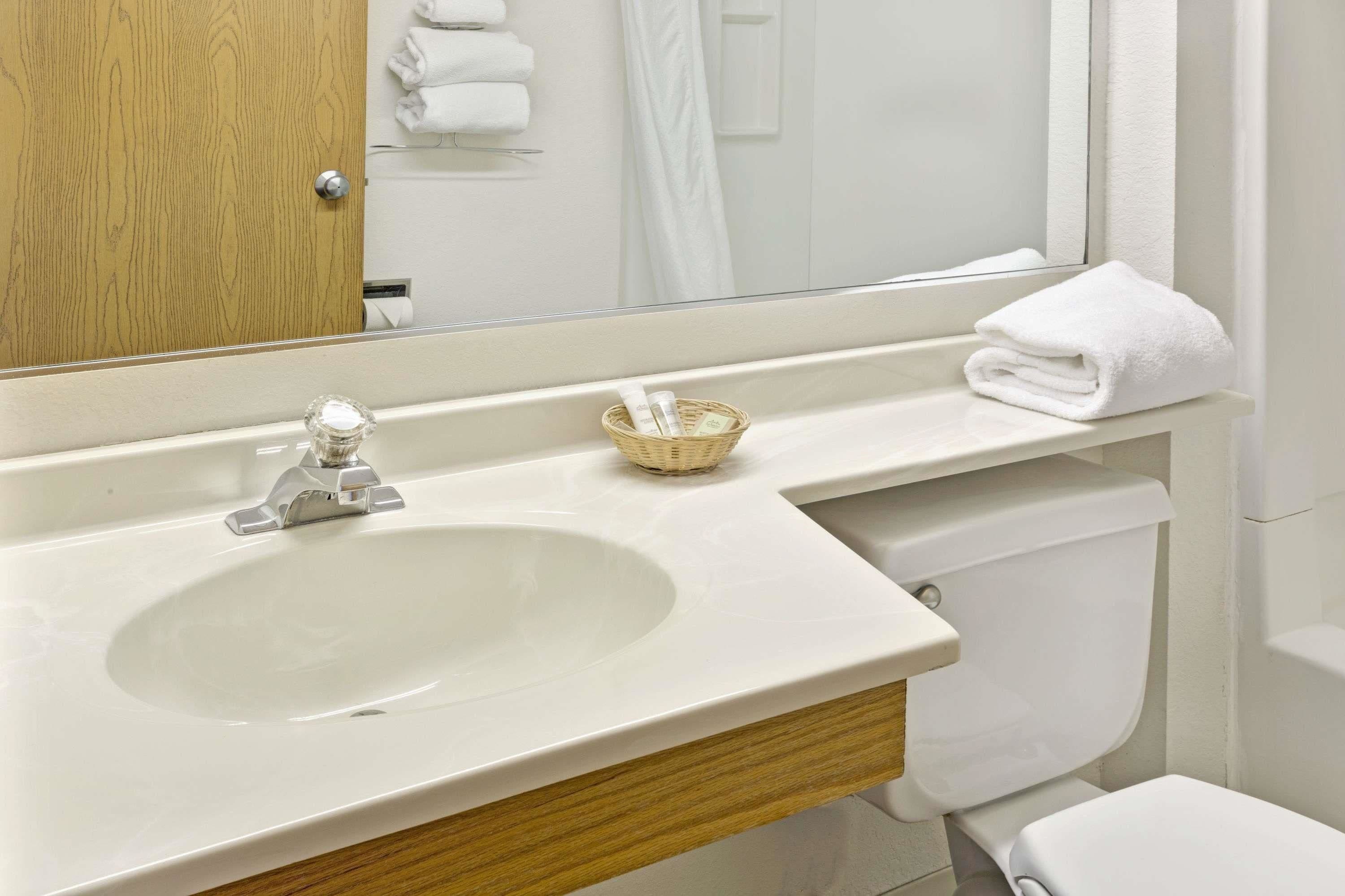 A bathroom with a white sink, a wooden vanity, a mirror, and a white towel on the counter.