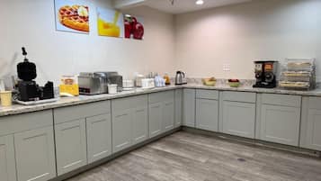 A kitchen with a granite countertop, a waffle maker, coffee machines, and a fruit bowl.