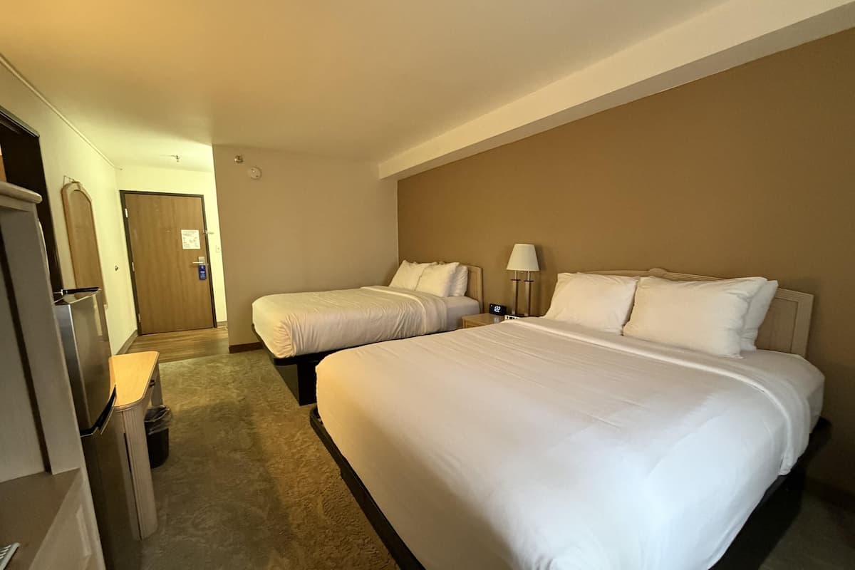 Ein Hotelzimmer mit zwei Betten, einem Schreibtisch, einem Papierkorb und einer Tür.