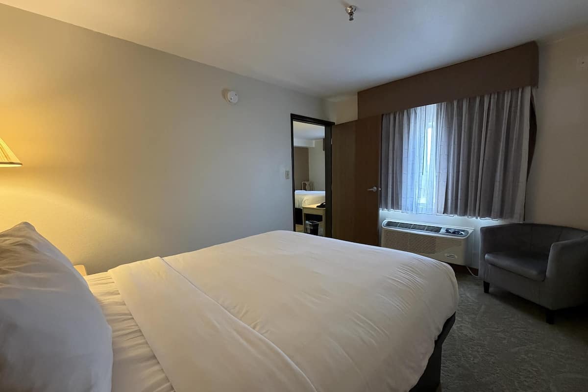 Ein Hotelzimmer mit einem großen Bett, einem Sessel, einem Schreibtisch und einem Fenster mit Vorhängen.
