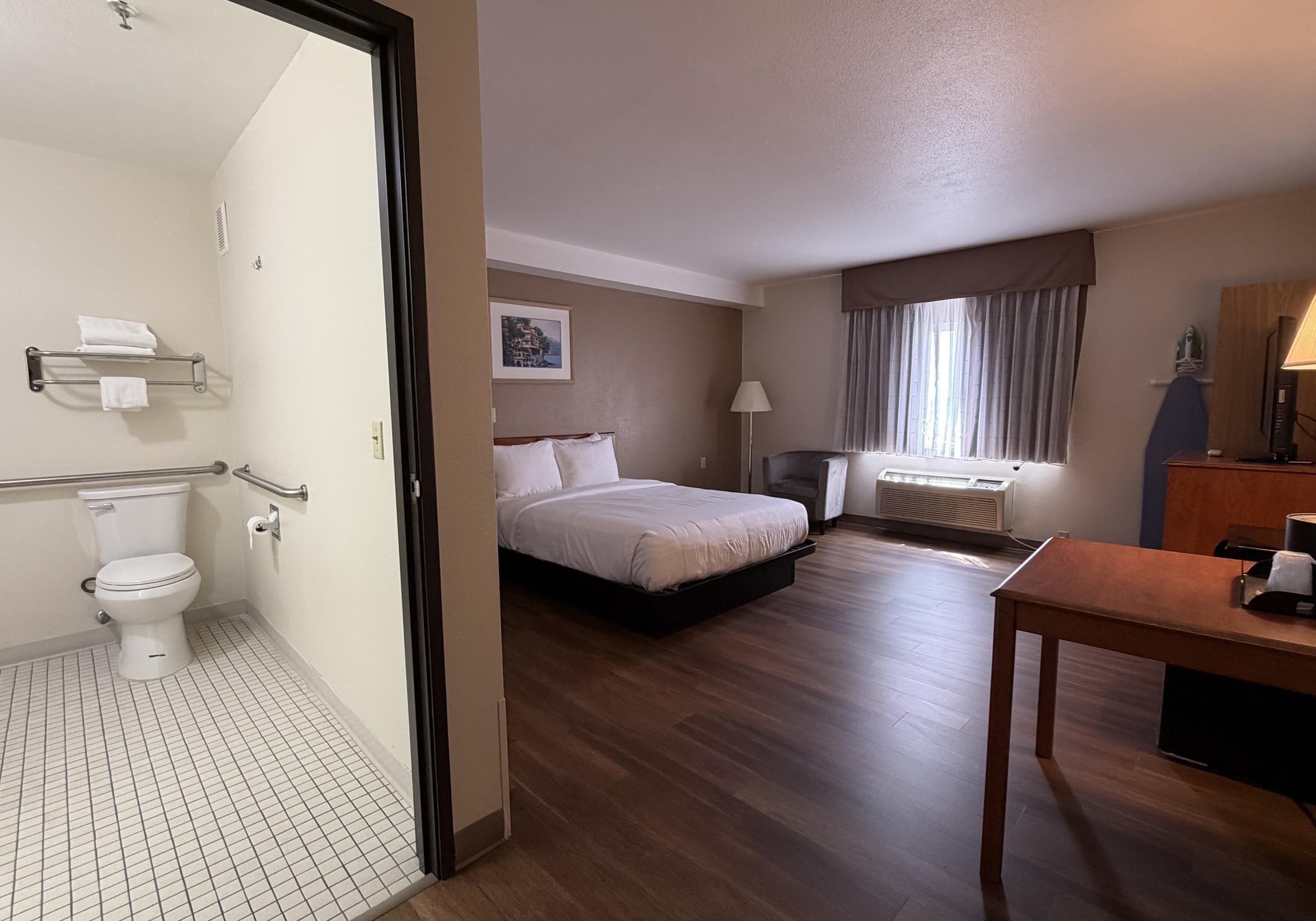 Une chambre d’hôtel avec un lit, une table de chevet, une lampe et une vue sur le paysage urbain par la fenêtre.