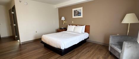 A hotel room with a bed, a chair, a nightstand, a lamp, and a painting on the wall.