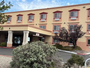 Un hotel de varios pisos con fachada color beige, marcos de ventanas rojos y un acceso cubierto.