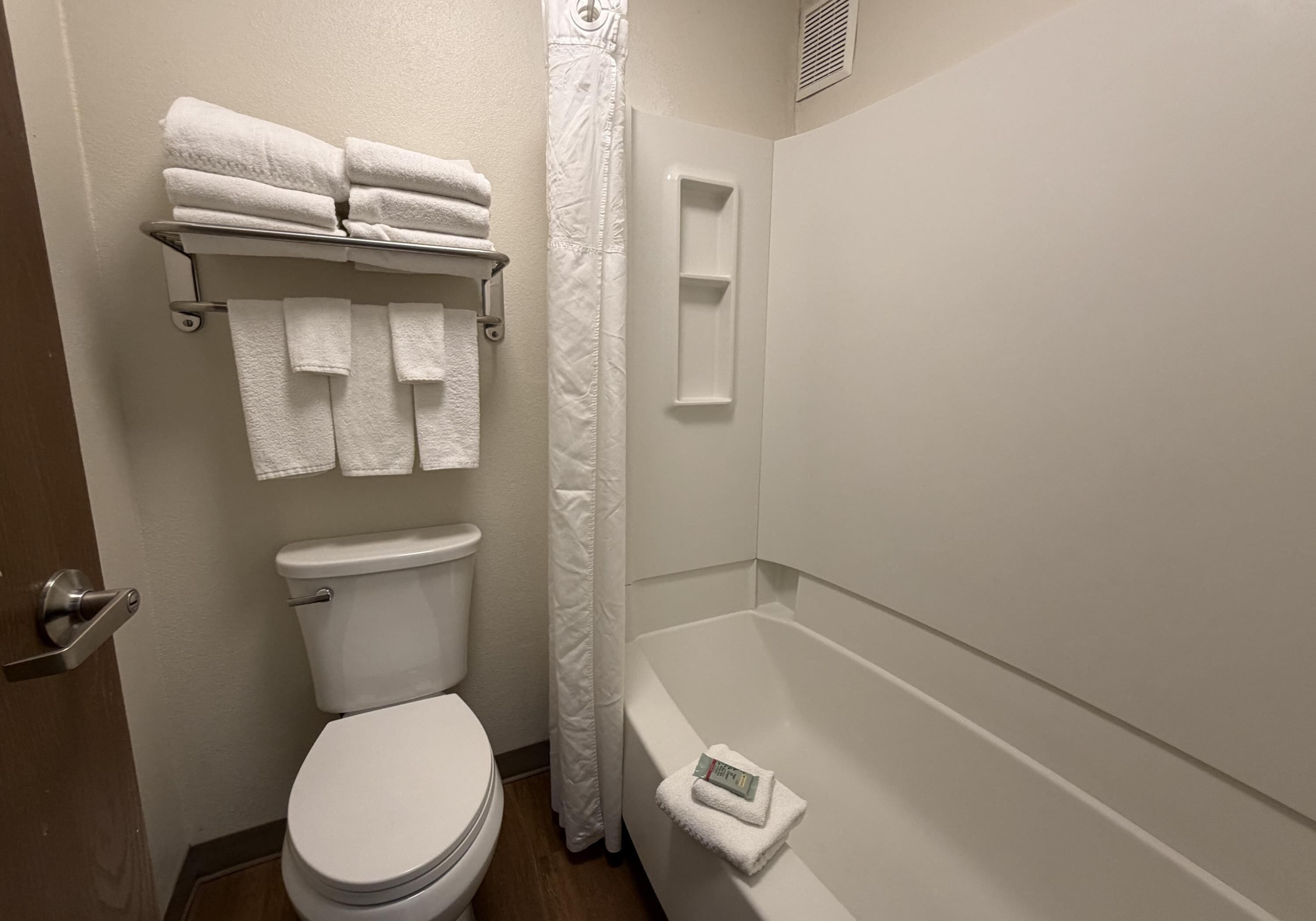 A bathroom with a toilet, a shower curtain, a bathtub, and a towel rack with folded towels.