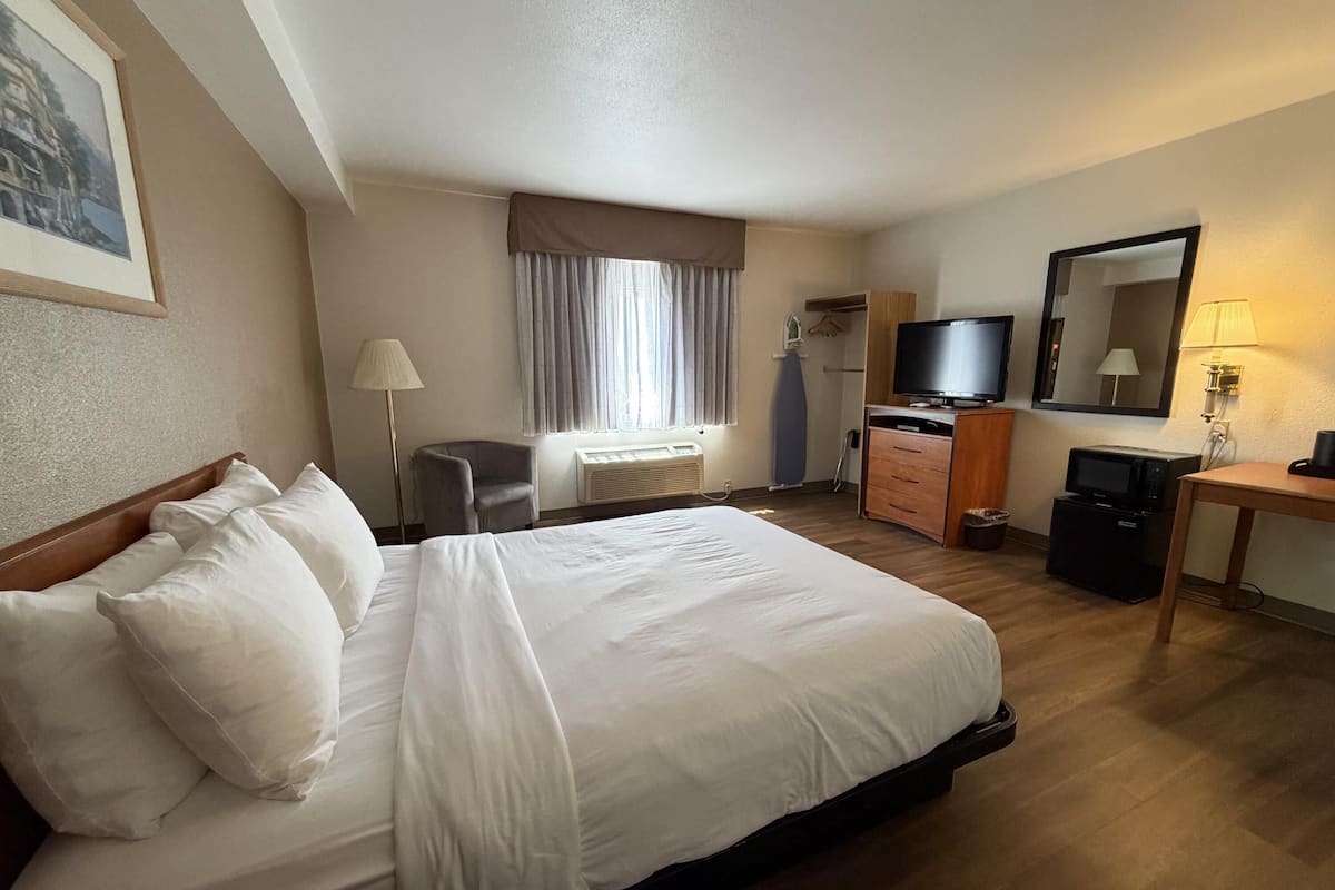 Ein Hotelzimmer mit Bett, Schreibtisch, Fernseher, Spiegel und einem Fenster mit Vorhängen.