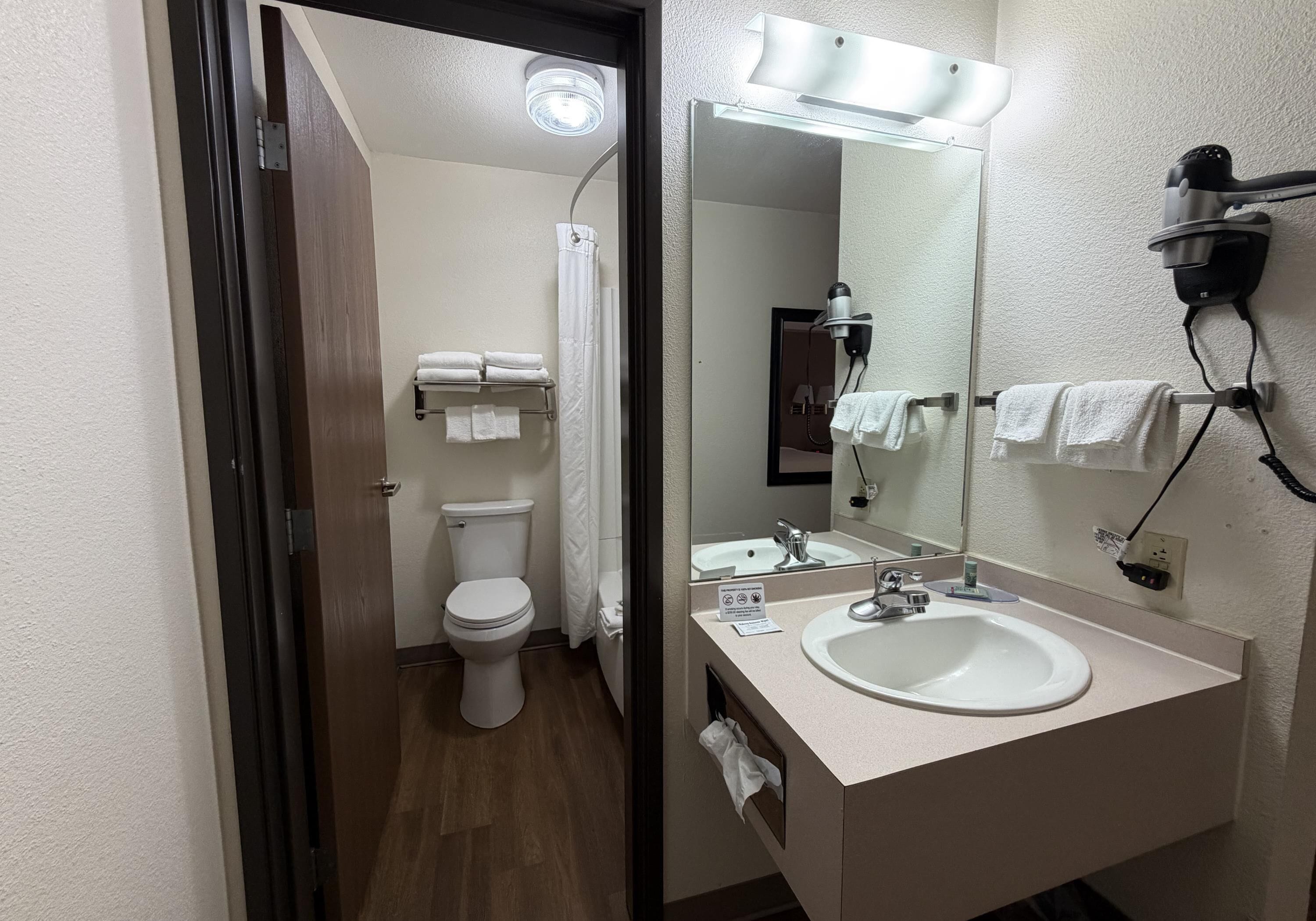 A bathroom with a toilet, sink, mirror, and hair dryer.