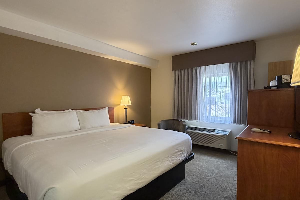 Ein Hotelzimmer mit einem großen Bett, einem Schreibtisch, einem Sessel, einer Lampe und einer Klimaanlage.