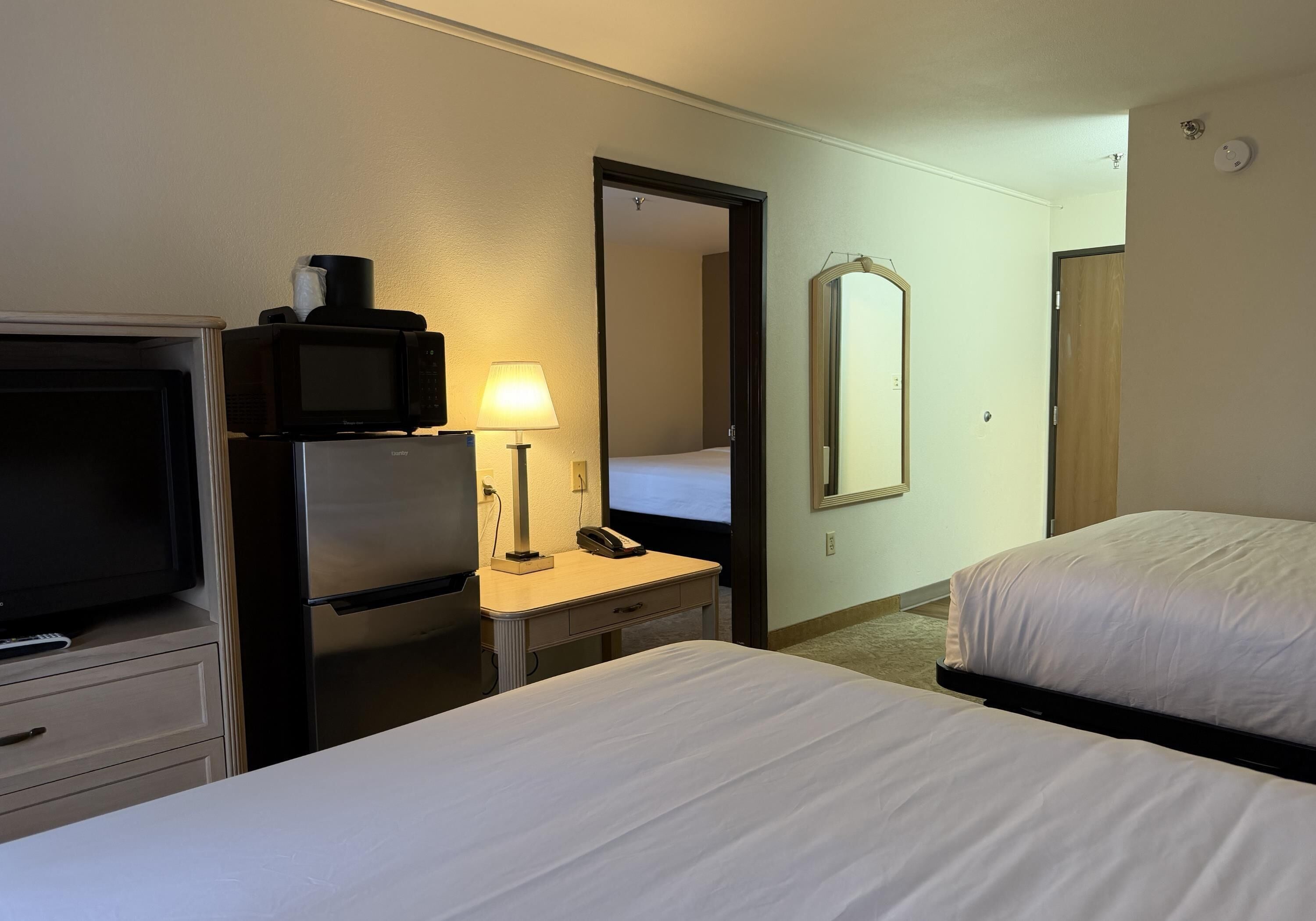 Habitación de hotel con cama, escritorio con lámpara, microondas, refrigerador, televisor y espejo.