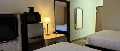 A hotel room with a bed, a desk with a lamp, a microwave, a refrigerator, a television, and a mirror.
