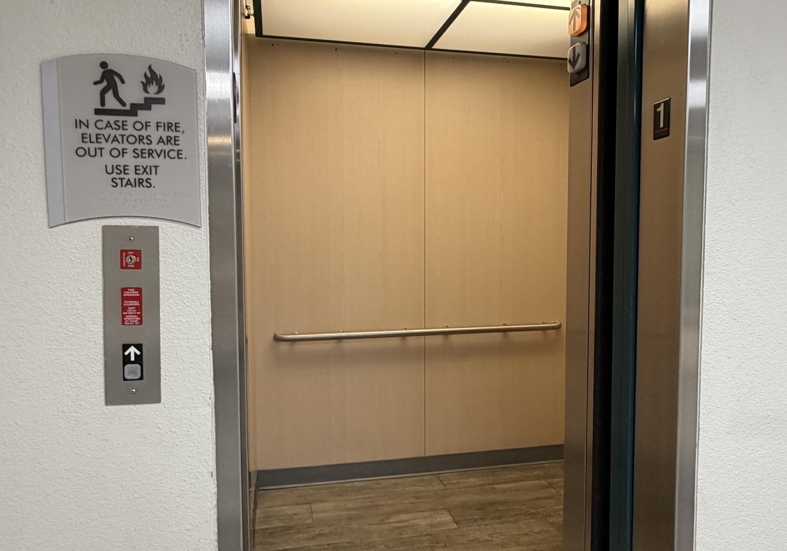 An elevator interior with a fire exit sign, a fire alarm button, and a directional arrow sign.