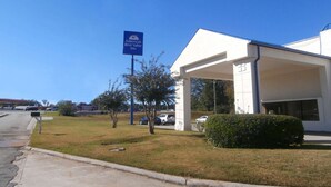 A hotel entrance with a sign for America's Best Value Inn, a covered parking area, and a grassy lawn with a few trees. - Americas Best Value Inn Tucker (Tucker)