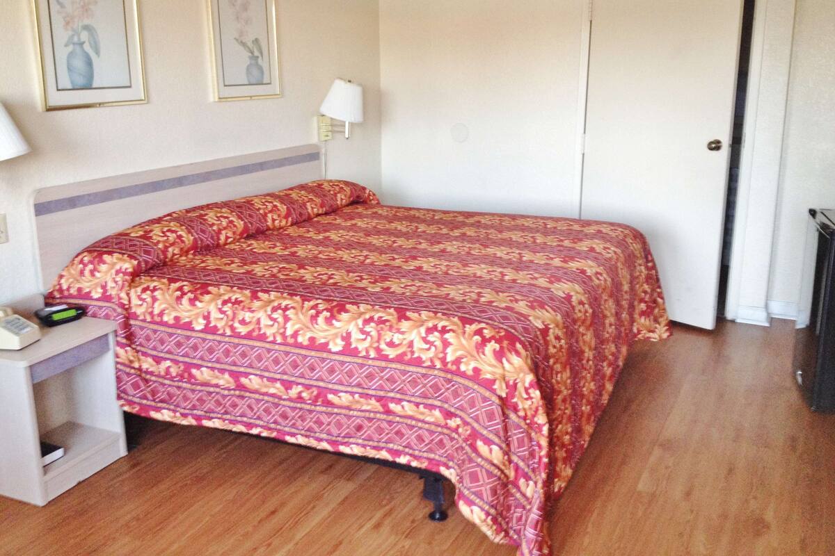 A neatly made bed with a patterned bedspread, a bedside table with a lamp, and two framed pictures on the wall.