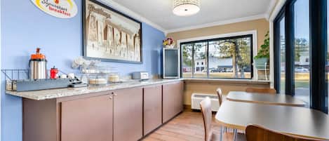 A modern kitchen with a breakfast bar, a large window, and a dining area with a table and chairs.