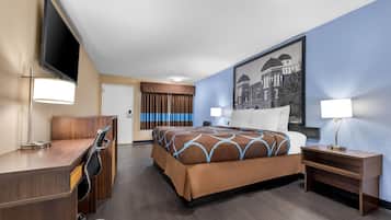 A hotel room with a bed, a desk, a chair, a TV, and a painting on the wall.