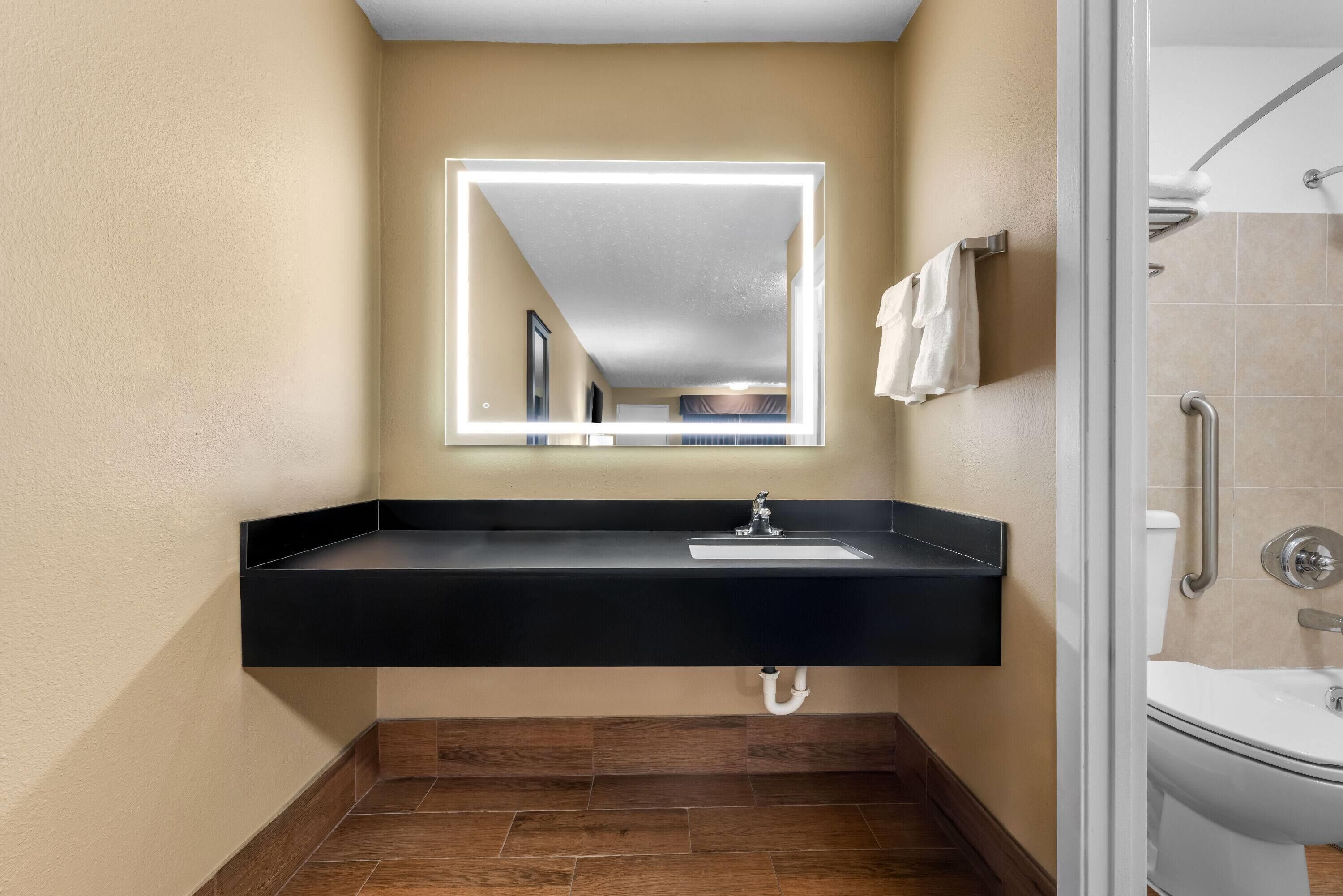 Une salle de bain avec un lavabo noir, un miroir avec éclairage intégré, une douche et des toilettes.