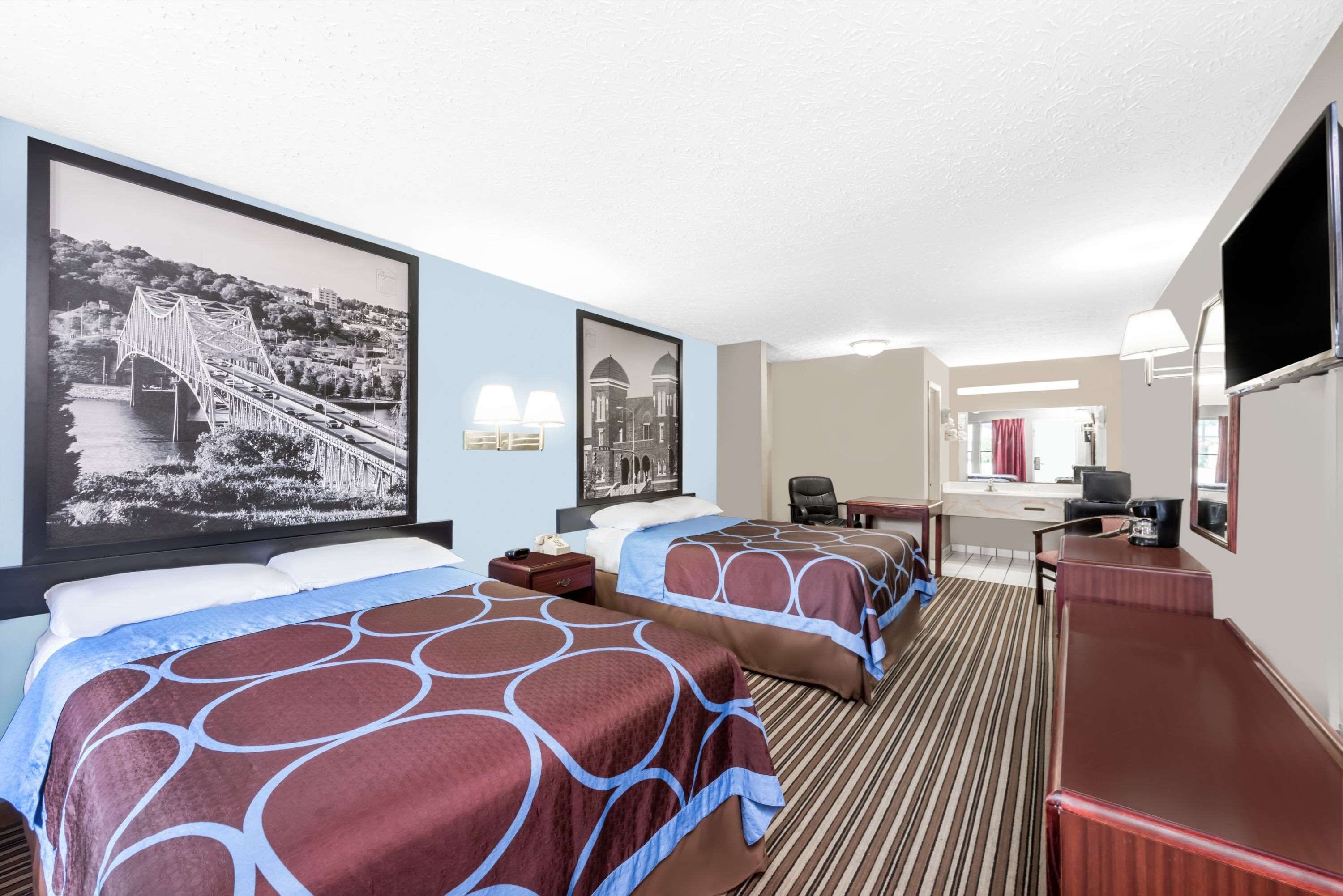 A hotel room with two beds, a desk, a chair, and a TV.