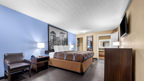 Habitación de hotel con cama, escritorio, silla, televisor y un cuadro en la pared.