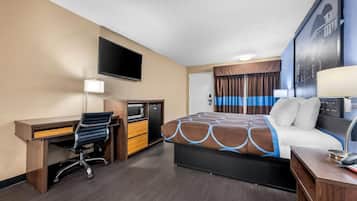 A hotel room with a bed, desk, chair, TV, and a small kitchenette.