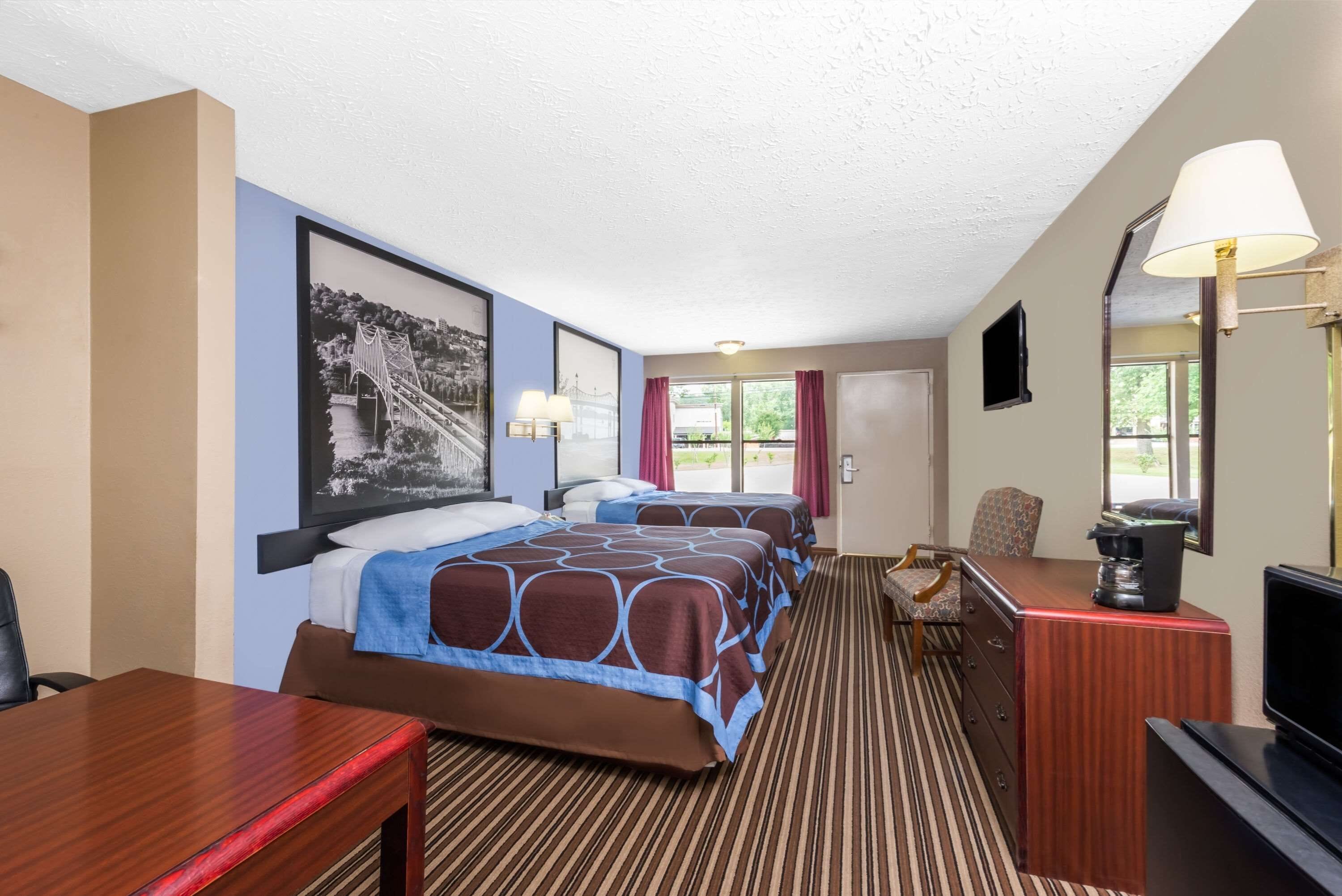 Ein Hotelzimmer mit zwei Betten, einem Schreibtisch, einem Stuhl, einem Fernseher und einem Fenster mit Vorhängen.
