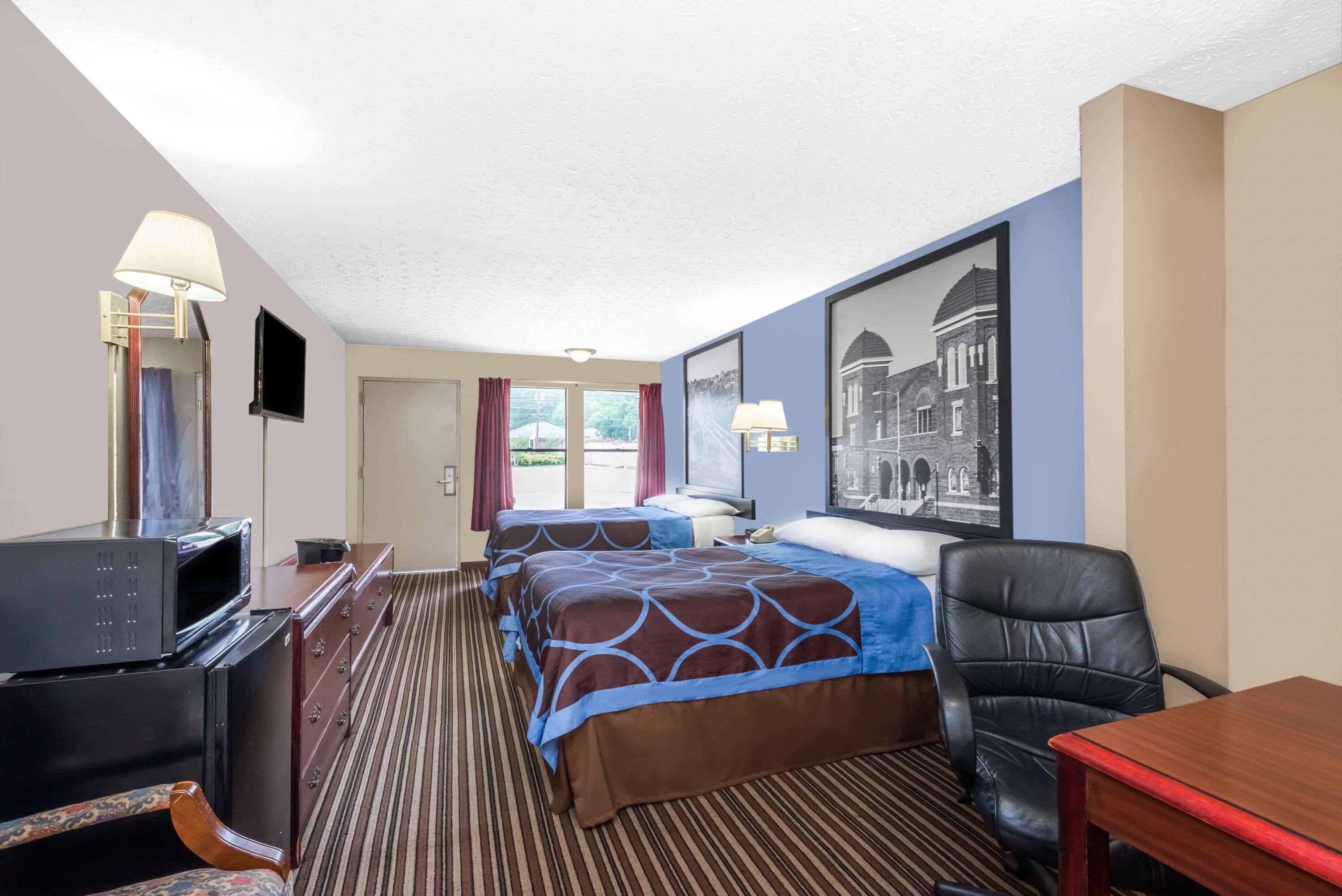 A hotel room with two beds, a desk with a computer, a TV, and a chair.