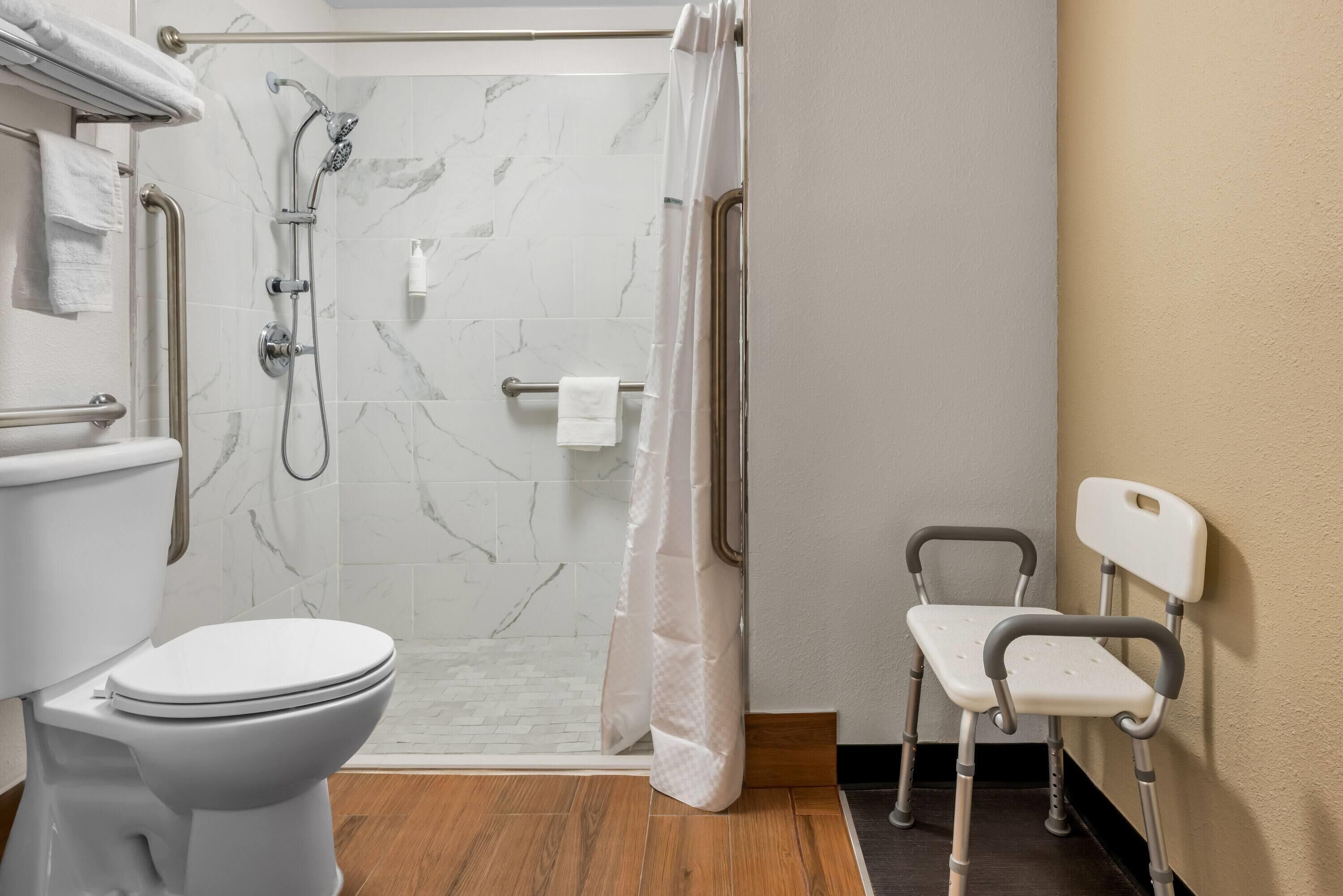 A bathroom with a toilet, shower, and a wheelchair-accessible chair.