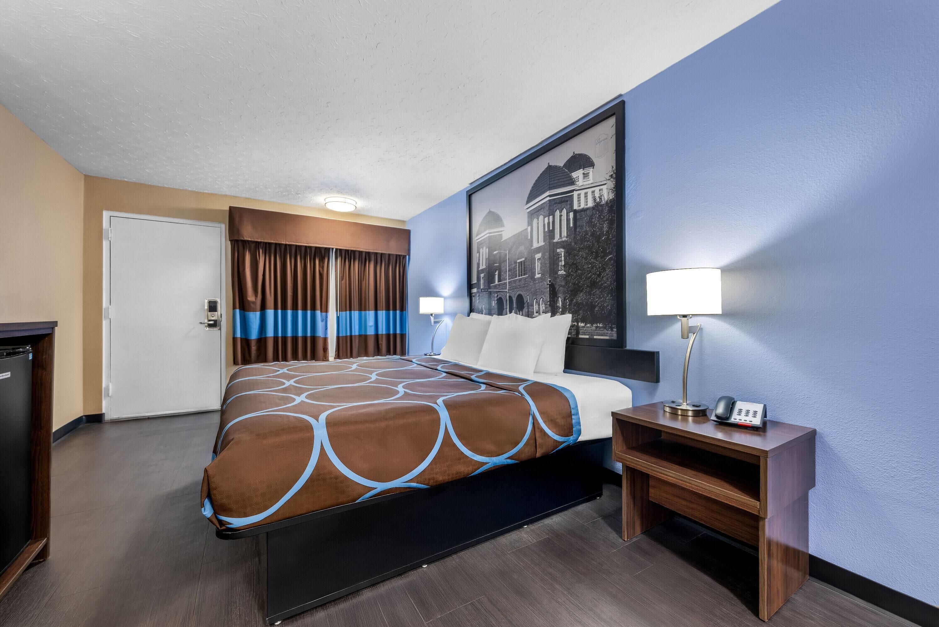 A hotel room with a bed, a desk with a lamp, a phone, and a picture on the wall.