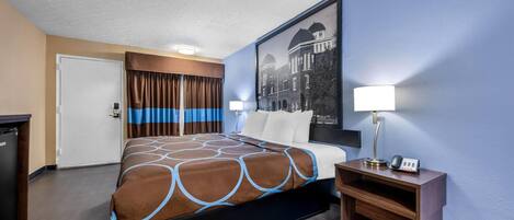 A hotel room with a bed, a desk with a lamp, a phone, and a picture on the wall.