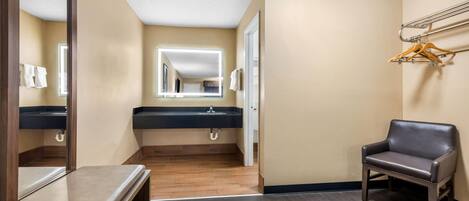A hotel bathroom with a wooden floor, a bench, a mirror, a sink, and a chair.
