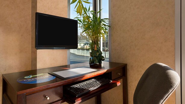 Un escritorio de madera con un monitor de computadora, teclado y una pequeña planta en maceta.