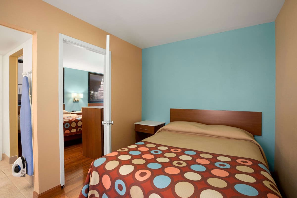 Una camera d'albergo con un letto, un comodino, una porta che dà su un'altra stanza e una vista sulla città attraverso la finestra.