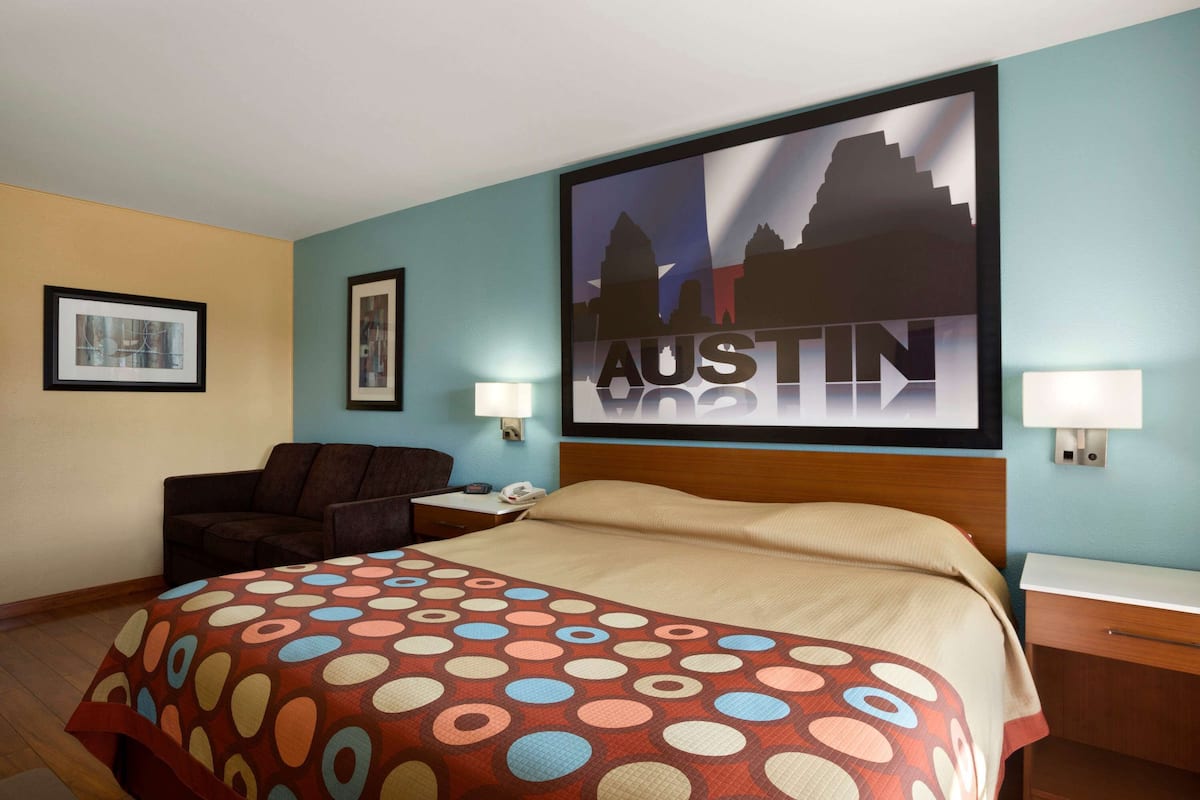 Una camera d'albergo con un letto, un comodino, una sedia e un quadro con una vista cittadina.