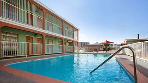 Una piscina con escalera de metal, rodeada por un edificio con balcones y techo rojo.