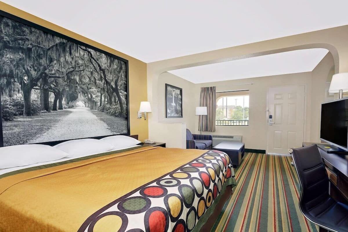 Een hotelkamer met een groot bed, een televisie, een bureau en uitzicht op bomen.