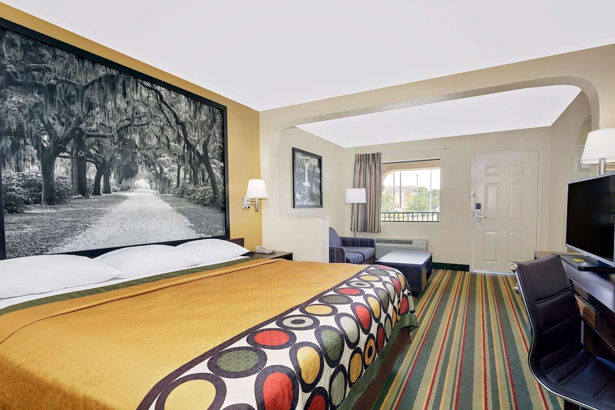 Een hotelkamer met een groot bed, een televisie, een bureau en uitzicht op een straat met bomen.