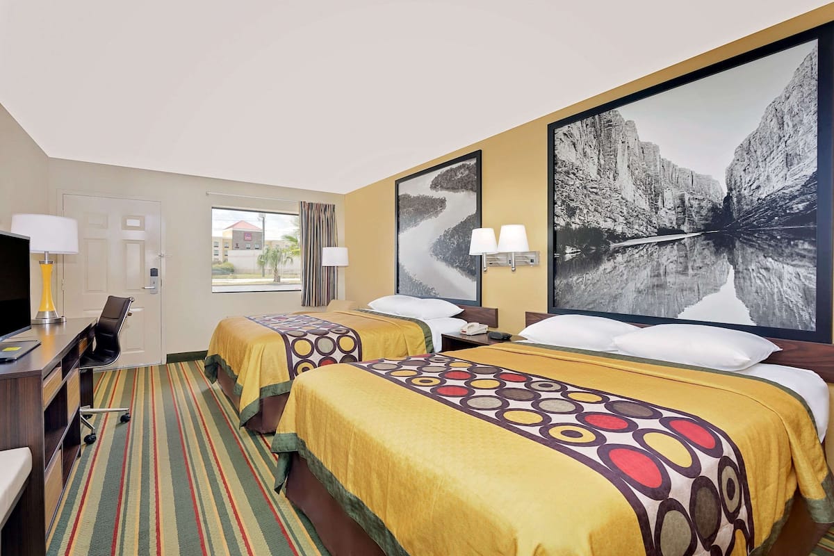 Een hotelkamer met twee bedden, een bureau met stoel, een televisie en een groot raam.