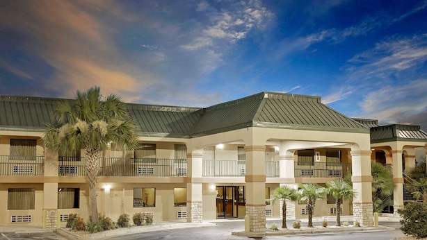 Ein mehrstöckiges Hotel mit modernem Design, mit Balkonen, einer überdachten Eingangshalle und einem begrünten Vorgarten mit Palmen.