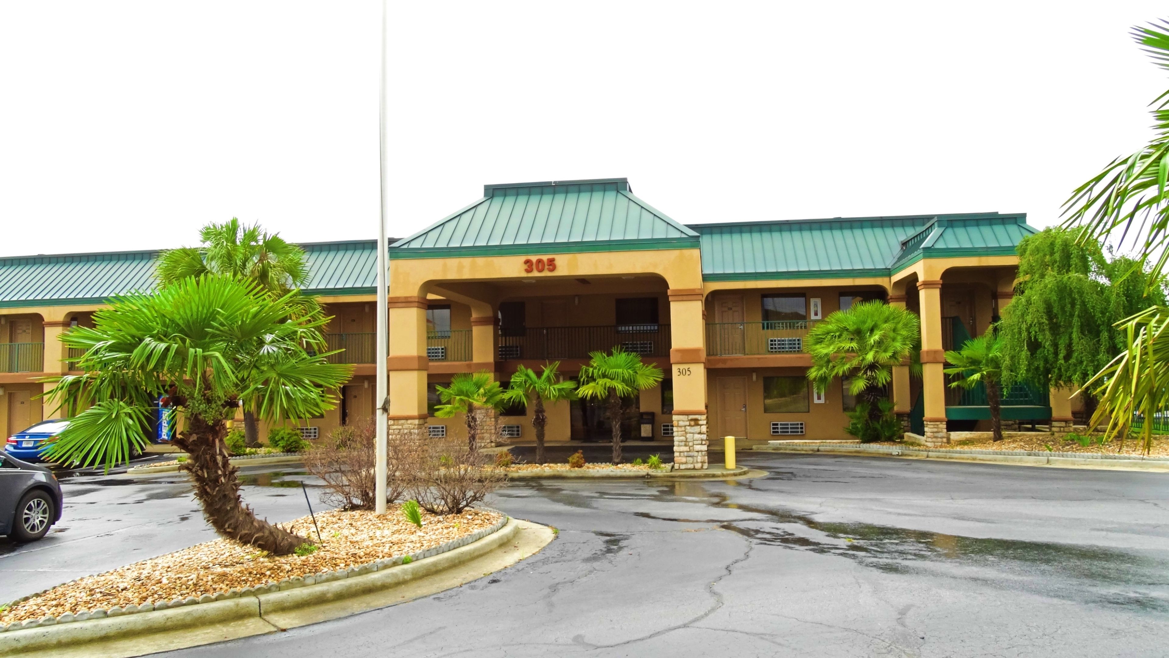 A hotel with a green roof, numbered 305, featuring a two-story structure with balconies and a parking lot in front.