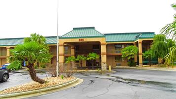 A hotel with a green roof, numbered 305, featuring a two-story structure with balconies and a parking lot in front.