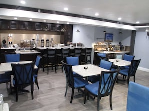 A modern restaurant with a bar area, multiple seating options, and a kitchen in the background.
