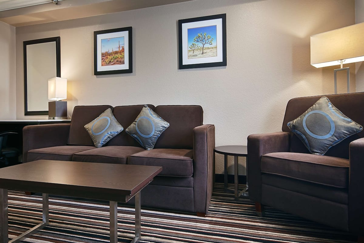 Une chambre d’hôtel avec un canapé marron, une petite table, une lampe et deux tableaux encadrés accrochés au mur.