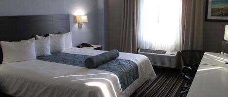 A hotel room with a large bed, a desk, a chair, a lamp, and a window with curtains.