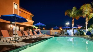 A nighttime pool area with lounge chairs and umbrellas, a swimming pool, and palm trees. - Best Western Plus Diamond Valley Inn (Hemet)